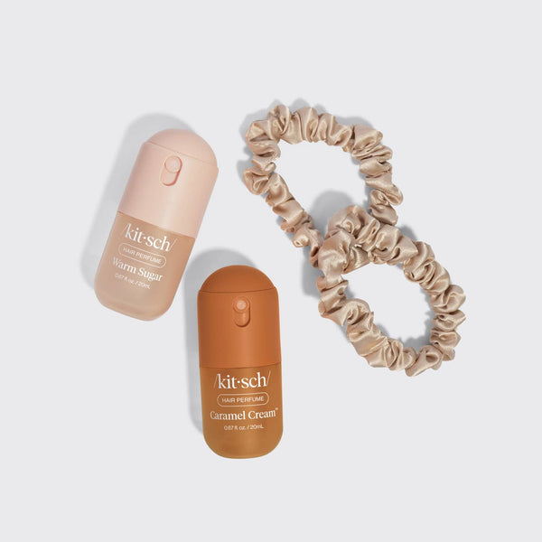 A flat-lay of a beauty kit featuring two Kit-Sch liquid eyeshadow pots (Warm Sugar in a pale peach cap and Gimmel Cream in a brown cap) alongside two matching satin scrunchies in warm beige and tan shades, all arranged on a light gray background.