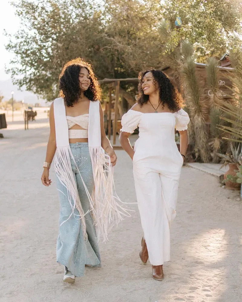 Two friends in cream and white outfits on a sunny desert road