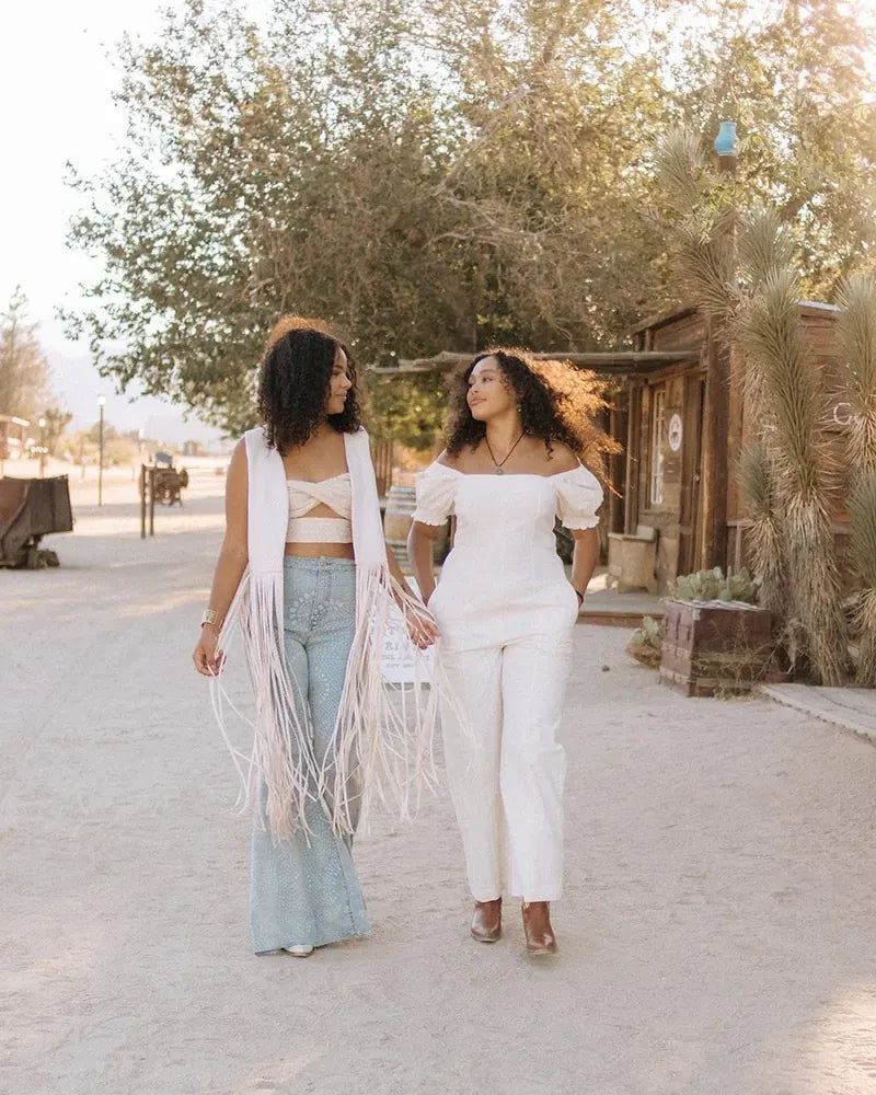 Two models in white fringe and denim walking down a desert road