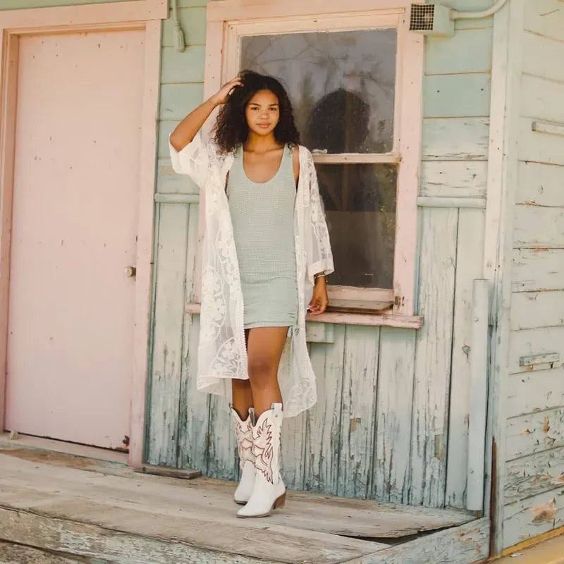 Model in a lace duster and white boots on a mint cabin porch
