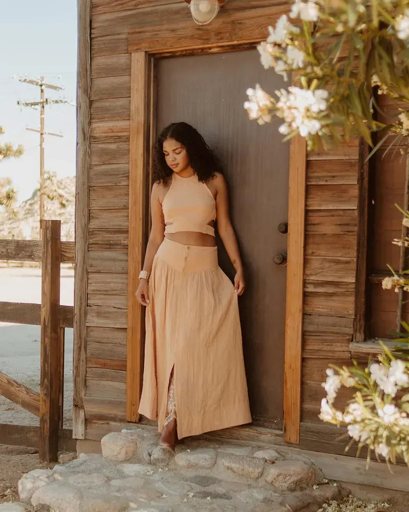 Model in a tan linen top and maxi skirt against a wooden door