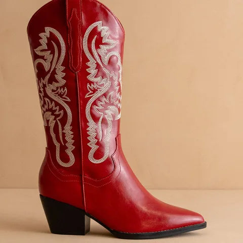 A single red leather cowboy boot with white embroidered western detailing on the shaft and a black block heel, shown against a solid beige background.
