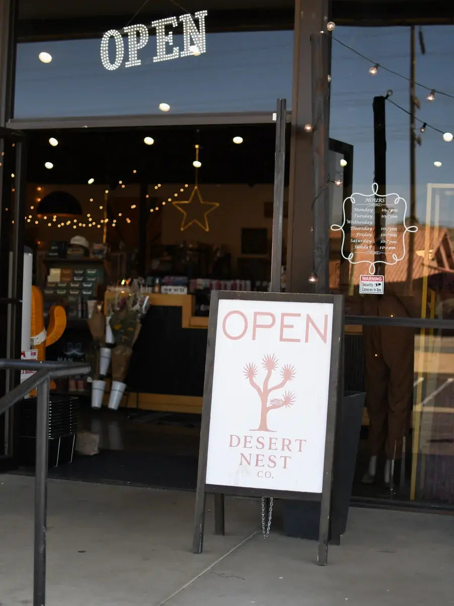 A storefront entrance with large glass windows and an outdoor A-frame sign reading 'OPEN' and 'DESERT NEST CO.' in front of the entrance.
